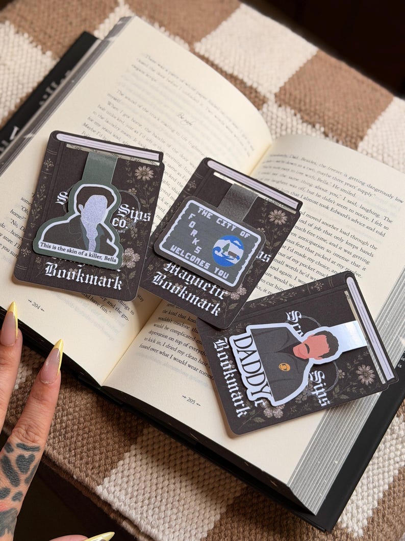 May include: Three rectangular magnetic bookmarks with dark floral backgrounds. One features a character illustration with the text 'This is the skin of a killer, Bella', another shows a 'The City of Forks Welcomes You' sign, and the third displays a character with the text 'Daddy'.