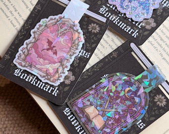 May include: Three magnetic bookmarks featuring holographic designs. One shows a dragon in a pink arched window, another a purple stained-glass scene with an open book, and the third a blue dragon with the text Hot Girls Read Fantasy.