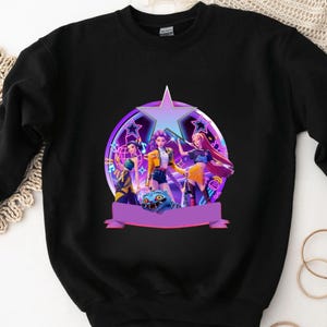 May include: Black sweatshirt with a colourful graphic of three animated characters inside a star-shaped frame. The design incorporates purple, yellow, and blue, with a banner at the bottom. The sweatshirt is made of a soft material.
