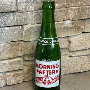 May include: A green glass bottle with a white label featuring the text "MORNING AFTER CHASER MIXER". The bottle also has the text "A GOOD DRINK" and "7 FL. OZS.". The label has a red and white graphic of a man.