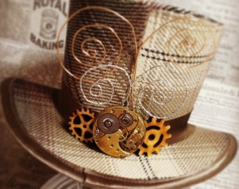 Puede incluir: Un sombrero de copa de cuadros marrones y blancos con un diseño steampunk. El sombrero tiene un diseño decorativo de engranaje metálico y esfera de reloj en la parte delantera.