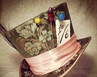 May include: A green and gold top hat with a pink ribbon and a white card with the text "1/6" on it. The hat has three pins with colorful beads on top.