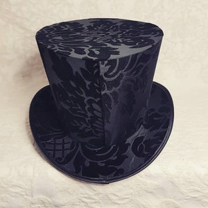 May include: A black top hat with a damask pattern. The hat has a tall, cylindrical crown and a wide brim.