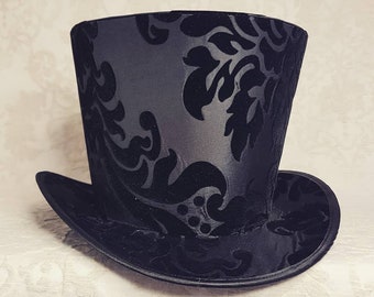 May include: A black top hat with a damask pattern. The hat is made of a smooth, silky fabric.