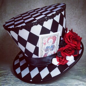 May include: A black and white checkered top hat with a black ribbon and a card featuring the Queen of Hearts from Alice in Wonderland. The hat is decorated with red roses.
