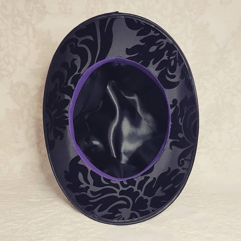May include: A black velvet hat with a purple satin trim and a black damask pattern.
