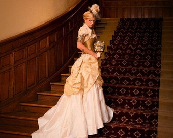 May include: A woman in a white and gold wedding dress with a gold and white floral bouquet stands on a staircase with a dark wood railing and a red patterned carpet.