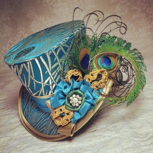 May include: A teal blue top hat with a peacock feather design and a gold and teal flower embellishment.
