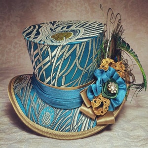May include: A teal and silver top hat with a peacock feather and a gold and teal flower embellishment.