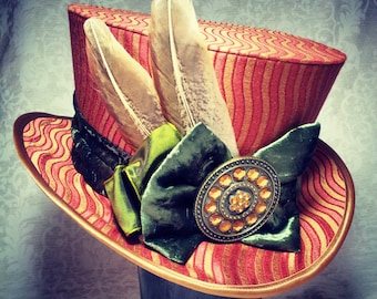 May include: A red and gold striped top hat with a green velvet bow and a gold jeweled embellishment. Two feathers are attached to the hat.
