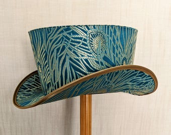 May include: A teal blue top hat with a gold and teal patterned design. The hat has a brown leather brim.