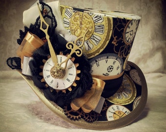 Puede incluir: Un sombrero de copa negro y dorado con un diseño de esfera de reloj y una aguja de reloj dorada. El sombrero está decorado con encaje y una cinta dorada.