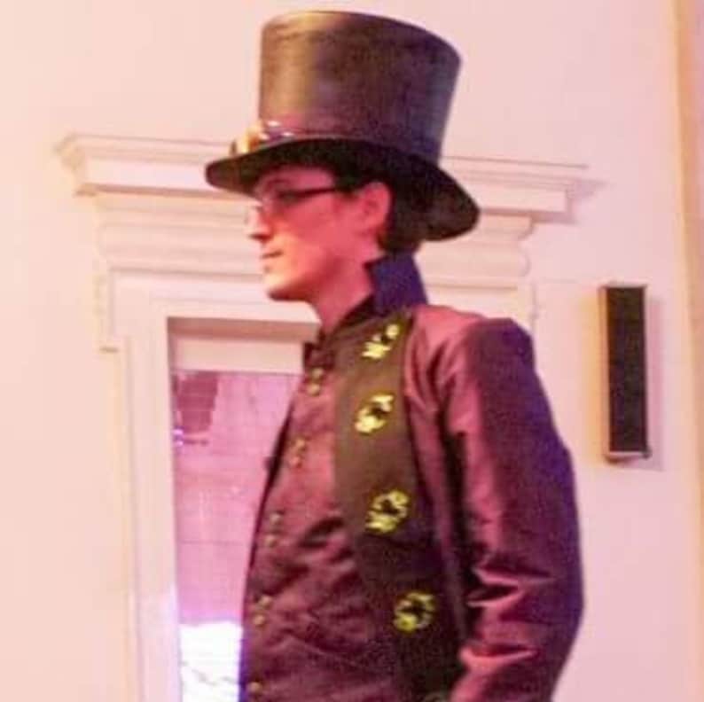 May include: A person wearing a black top hat with goggles, a black jacket, and a black and green scarf with a repeating design.