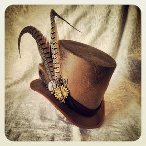 May include: A brown top hat with a distressed leather finish and a decorative gear and feather embellishment.