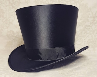 May include: A black top hat with a smooth, satin-like finish and a matching black grosgrain ribbon band encircling the base of the crown. The hat features a tall, cylindrical crown and a curved brim that extends outward from the base.