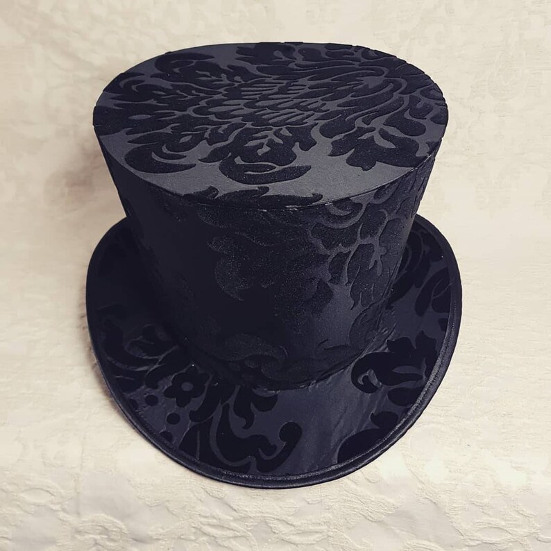 May include: A black top hat with a damask pattern. The hat is made of a soft, velvety material.