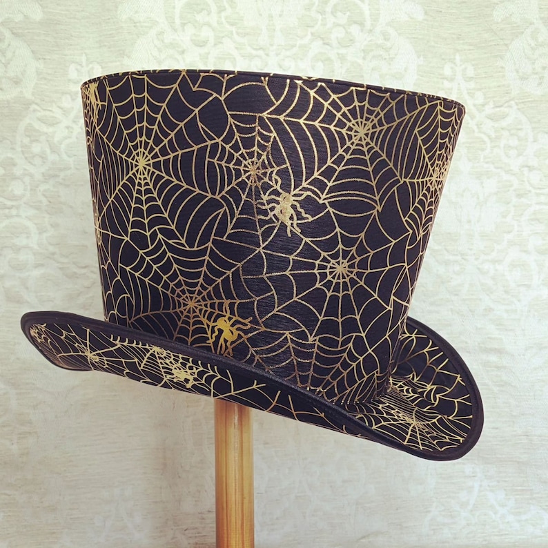 May include: A black top hat with a gold spiderweb pattern. The hat has a wide brim and a tall crown.