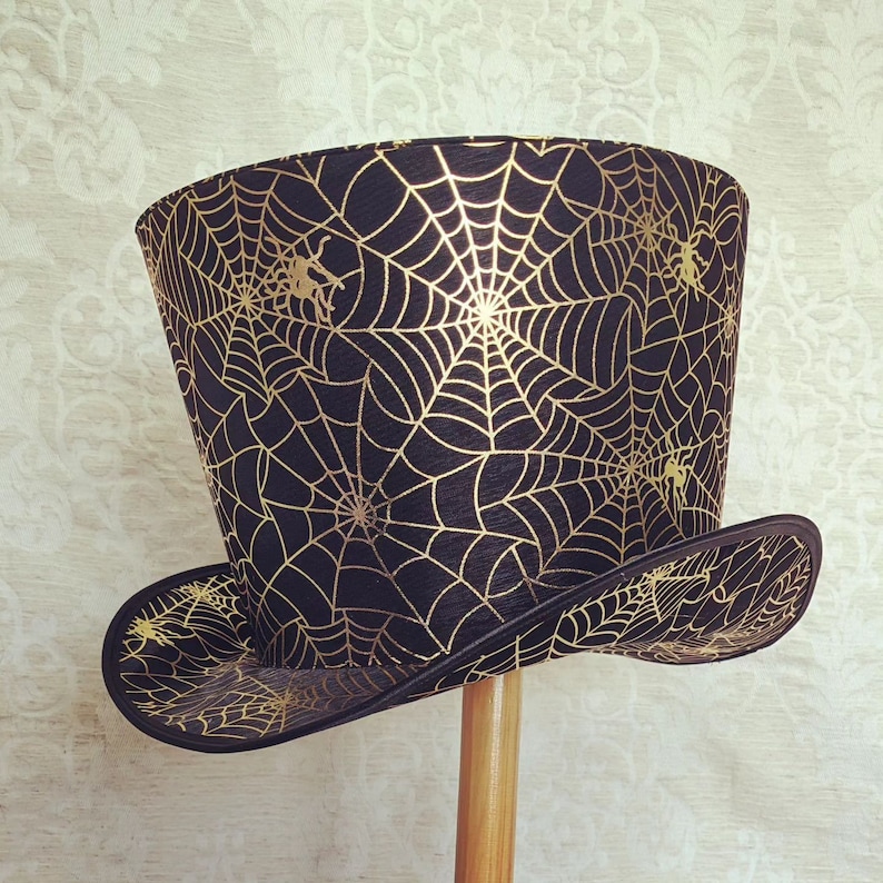 May include: A black top hat with a gold spiderweb pattern. The hat has a wide brim and a tall crown.