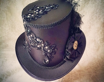 Può includere: Un cappello a cilindro nero con un ricamo in pizzo nero e strass, un fiocco di raso nero e una piuma nera.