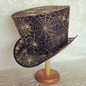 May include: A black top hat with a gold spiderweb pattern. The hat is on a wooden stand.