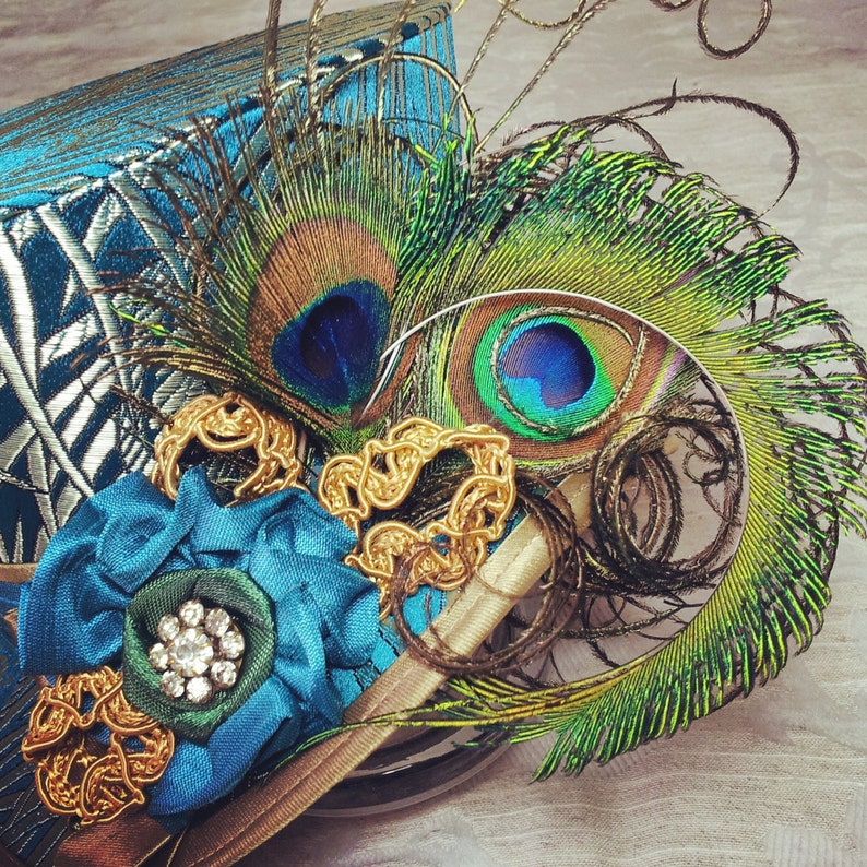 May include: A blue and gold hat with a peacock feather design. The hat is decorated with gold trim and a blue flower.
