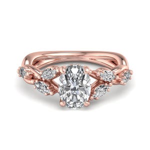 Puede incluir: Un anillo de oro rosa con una piedra preciosa central transparente de corte ovalado sujeta por cuatro garras. La banda presenta un diseño de enredadera, adornado con cuatro piedras transparentes de corte marquesa a cada lado del engaste.