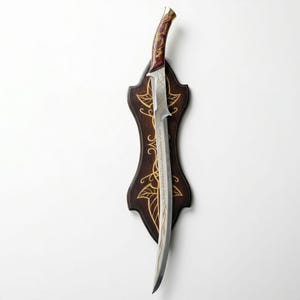 May include: A decorative sword with a curved blade and a wooden handle. The handle is burgundy with gold accents. The blade has gold etched designs and is mounted on a dark brown wooden plaque with gold leaf patterns.