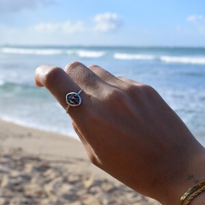 Peut inclure: Une bague en argent dotée d'un petit sertissage de forme ovale avec une pierre tachetée noire et blanche. L'anneau est fin et métallique, porté sur un doigt. Le design est simple, soulignant le contraste entre la pierre sombre et l'argent.