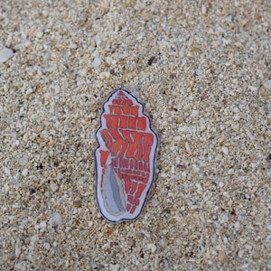 May include: A flat, translucent acrylic charm shaped like a spiral seashell. The shell features a vibrant orange and red geometric pattern with a grey, elongated opening at the base. The charm has a clear border and a small hole at the top for hanging.
