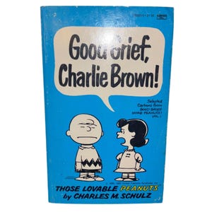 May include: A vintage paperback book titled "Good Grief, Charlie Brown!" features a blue cover with the title in a speech bubble. The cover includes illustrations of Charlie Brown and Lucy, with the text "Those Lovable Peanuts" and the author's name.