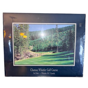 以下が含まれることがあります： シャトーウィスラーゴルフコースの額入りプリント。緑色のフェアウェイと森林の背景が特徴です。カナダ、ブリティッシュコロンビア州ウィスラーにあるコースの3番ホールが写っており、黄色の旗が見えます。フレームは濃い青色です。