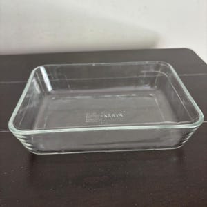 May include: A clear, rectangular glass baking dish with rounded corners and a smooth rim. The bottom of the dish features the embossed text PYREX, which is visible through the transparent glass, indicating the brand and material of the item.