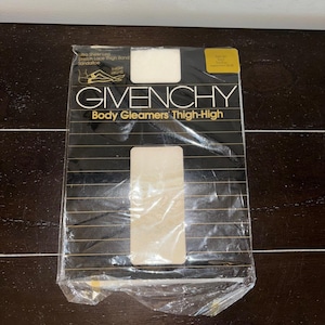May include: A black and gold Givenchy Body Gleamers Thigh-High stockings package. The packaging features the brand name and product description in gold lettering. The text "Ultra Sheer Leg, Stretch Lace Thigh Band, Sandallce" is also visible. The package is sealed in clear plastic.