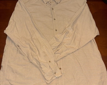 Puede incluir: Una camisa abotonada a cuadros beige y blanco con mangas largas. La camisa tiene un cuello abotonado y un pequeño logotipo en el pecho. La camisa está hecha de una tela ligera, adecuada para ropa casual.