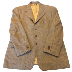 May include: A tan and brown herringbone blazer featuring a notched lapel, three front buttons, and three buttons on each sleeve cuff. The interior is lined with a solid gold-colored fabric, and the garment has two side pockets with flaps.