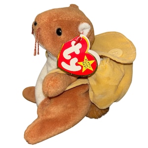 May include: A brown plush toy beaver with a yellow backpack and a red heart-shaped tag. The tag reads "Beanie Original Baby" in white text. The beaver has black eyes, a white belly, and brown whiskers.