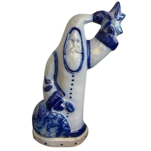 Puede incluir: Figura de cerámica de Papá Noel en blanco y azul. La figura sostiene una estrella azul y tiene una larga barba blanca. La figura tiene una base redonda y está decorada con detalles azules.