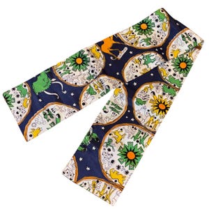 May include: A navy blue scarf with a repeating pattern of circular designs featuring various animals, suns, and stars. The circles are outlined in a tan color, with green, yellow, and white details. The background is navy blue.