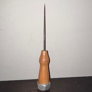 May include: A metal awl with a wooden handle and a silver base. The awl has a long, pointed tip and is designed for piercing or making holes in materials like leather or fabric. The handle is light brown.