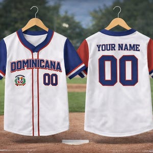 May include: White baseball jersey with blue and red accents. The front displays "DOMINICANA" and the number "00". The back features "YOUR NAME" and the number "00". The jersey has a Dominican Republic flag patch.