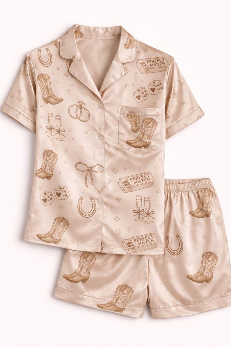 May include: A light beige pajama set with a button-down shirt and shorts. The set is patterned with cowboy boots, horseshoes, dice, champagne flutes, and the text "PERFECT MATCH".