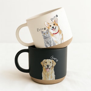 Może przedstawiać: Dwa ceramiczne kubki ułożone jeden na drugim. Górny kubek jest w kolorze złamanej bieli z ilustracją corgi i szarego kota, na kubku widnieją imiona "Milo" i "Bella". Dolny kubek jest czarny z ilustracją złotego retrievera i imieniem "Goose".