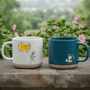 Może przedstawiać: Dwa ceramiczne kubki. Jeden jest biały z kreskówkowym gołębiem i napisem "I NEED COFFEE!!!". Drugi jest morski z grafiką kaczki i napisem "Mrs. Emily". Oba mają beżową podstawę i uchwyt.