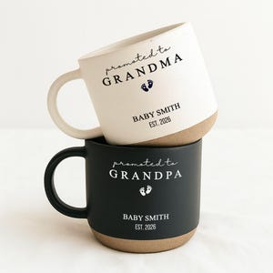 Peut inclure: Deux mugs en céramique, un blanc et un noir, empilés. Le mug blanc indique "promu GRAND-MÈRE" avec des empreintes de bébé et "BABY SMITH EST. 2026." Le mug noir indique "promu GRAND-PÈRE" avec des empreintes et "BABY SMITH EST. 2026."