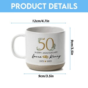 May include: A white ceramic mug with a beige base, featuring gold-colored "50" with floral accents, "Happy Anniversary", and names "Laura & Kenny". The mug is 3.5 inches wide, 3.5 inches tall, and 4.7 inches wide.