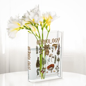 May include: A clear rectangular vase with the word "HERBOLOGY" printed in gold. The vase contains white and yellow flowers and illustrations of plants. The text "HOGWARTS SCHOOL OF WITCHCRAFT AND WIZARDRY" is printed at the bottom.