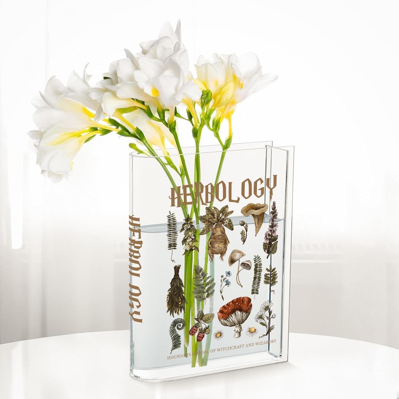 May include: A clear rectangular vase with the word "HERBOLOGY" printed in gold. The vase contains white and yellow flowers and illustrations of plants. The text "HOGWARTS SCHOOL OF WITCHCRAFT AND WIZARDRY" is printed at the bottom.