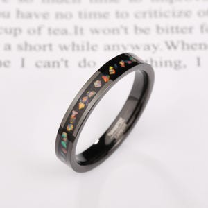Peut inclure: Une bague en carbure de tungstène noir avec une bande d'incrustation d'opale colorée. La bague a une finition polie et un design élégant et moderne. La bague est de taille 54.