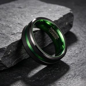 Op de afbeelding: Een zwarte ring van wolfraamcarbide met een geborstelde matte buitenkant, een dunne, felgroene groef in het midden en een gepolijste groene binnenkant. De binnenzijde van de ring is voorzien van de gravure TUNGSTEN CARBIDE.