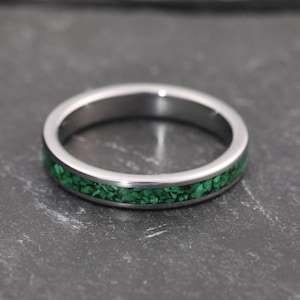 Peut inclure: Une bague argentée ornée d'une incrustation de pierres vertes éclatantes. La bague est circulaire et repose sur une surface sombre et texturée. Le design de la bague est simple, mais attrayant.